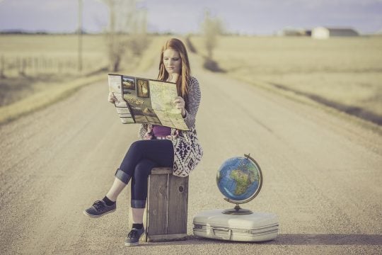 a person sitting in the middle of a road holding a map with an earth globe on the floor beside them