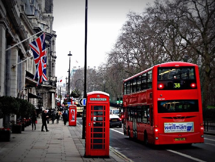 Red London bus passing telephone box and house with flag of Great Britain.